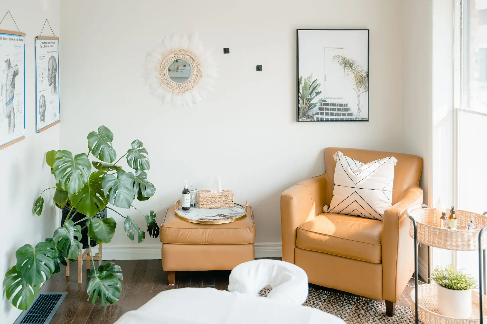 A bright Renu treatment room with a tan leather armchair, a monstera plant and a treatment table