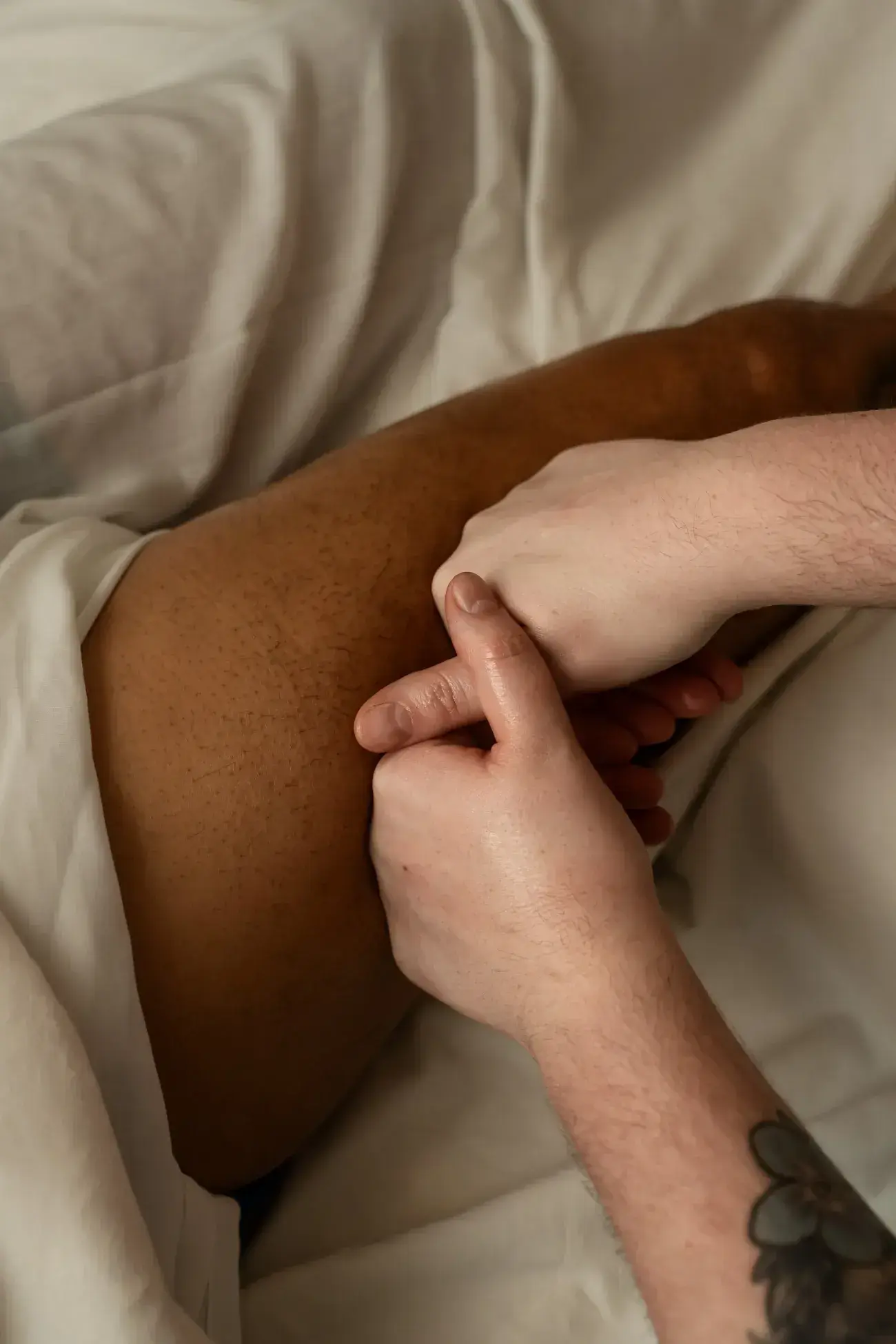 A therapist pressing both thumbs slowly into the muscle of a client's thigh during a massage at Renu