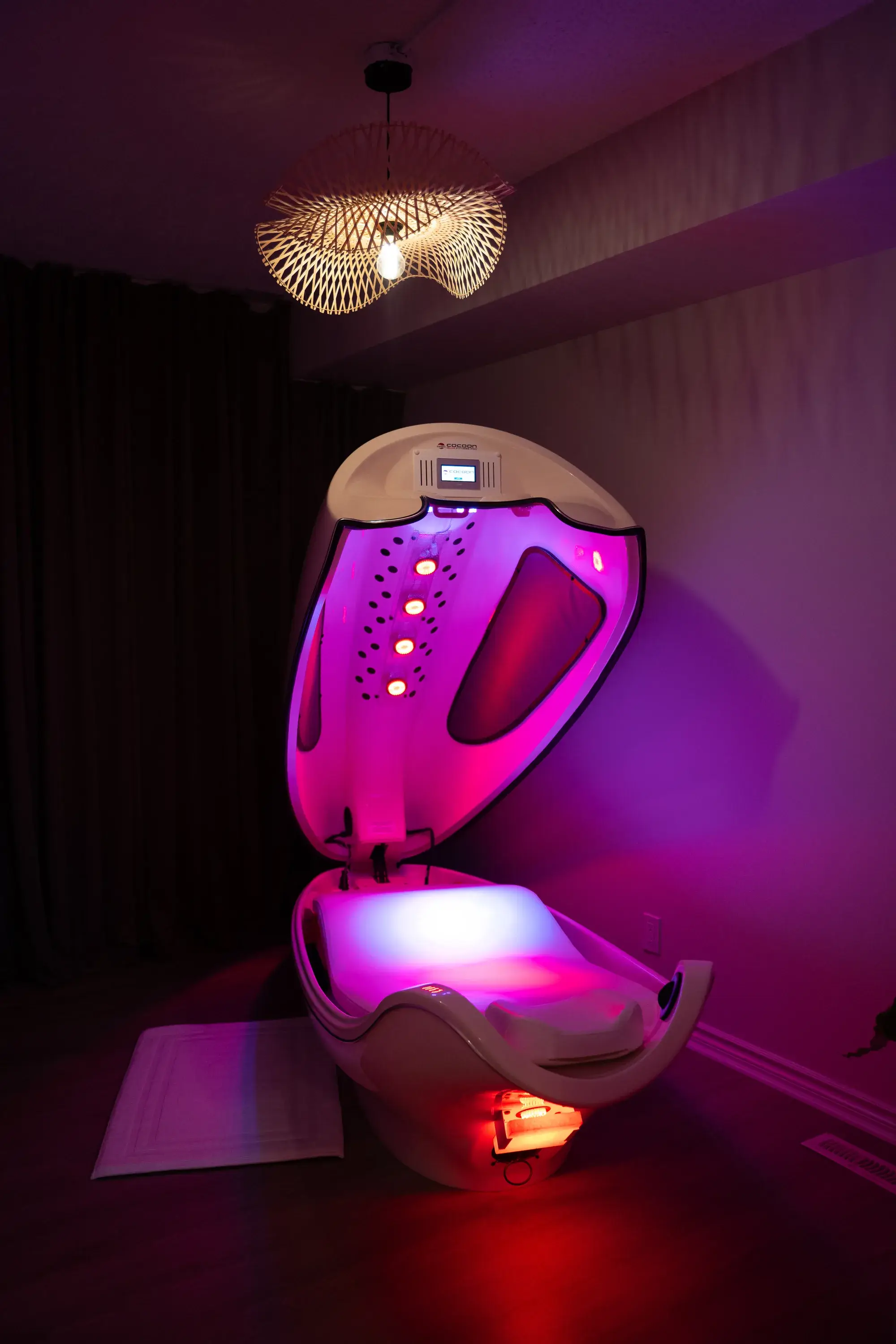 The infrared cocoon pod at BodyTox by Renu standing open in its dim room, lit from inside in pink and red