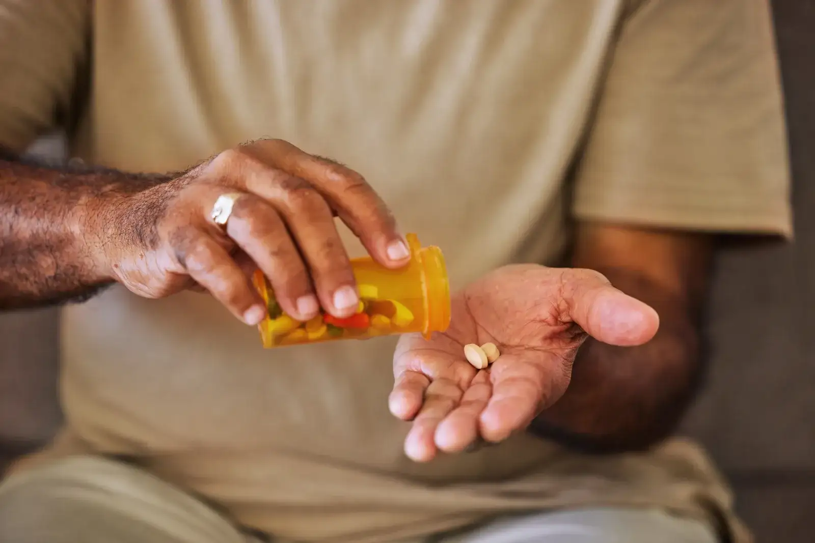A man tipping two tablets from an orange prescription bottle into his open palm