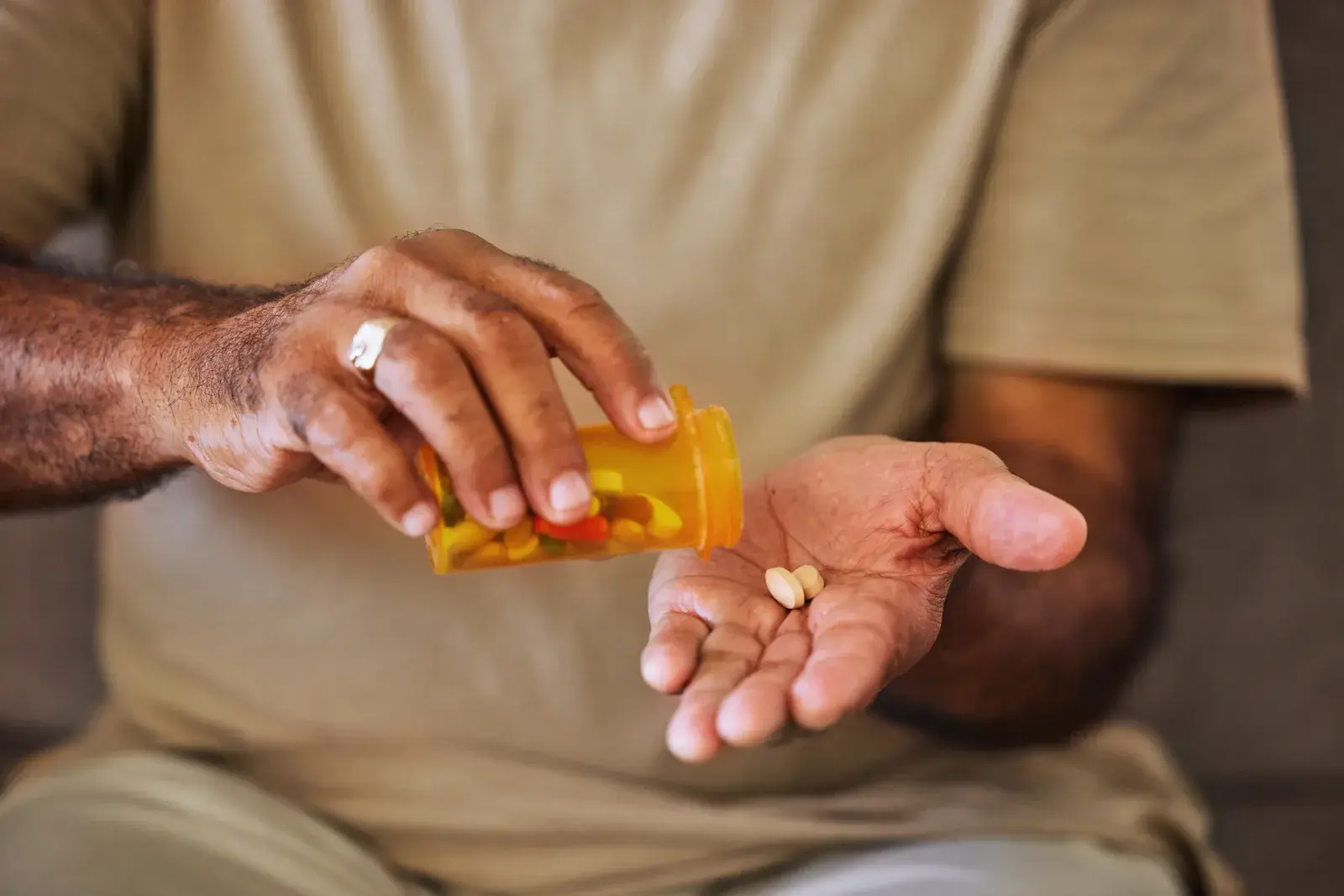 A man tipping two tablets from an orange prescription bottle into his open palm