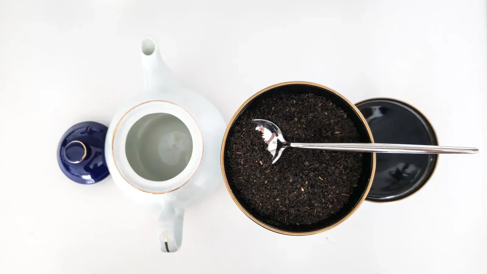 A white porcelain teapot, a cup and a tin of loose-leaf black tea seen from above on a white table