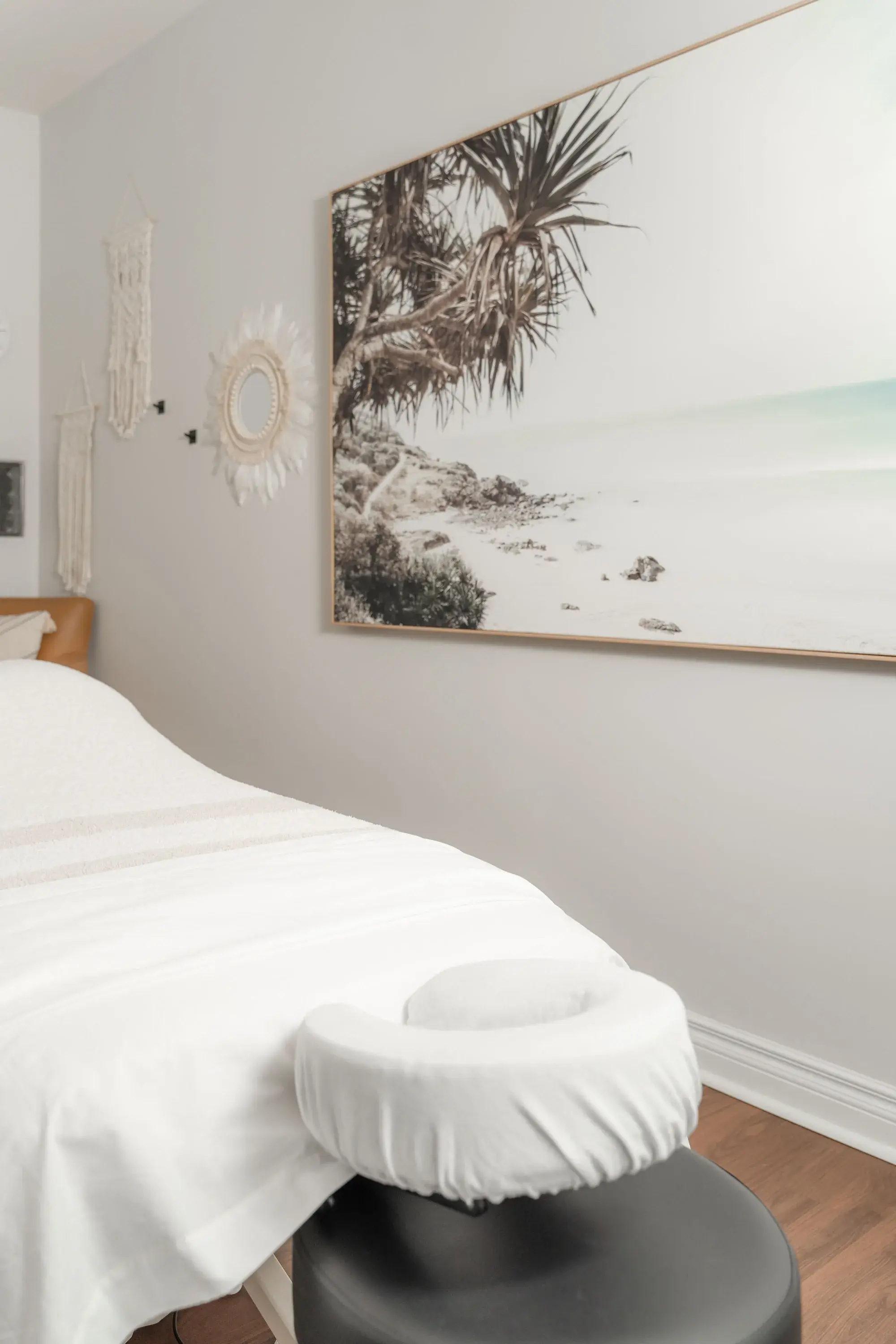 An empty treatment table dressed in white linen with its padded face cradle, beneath a seascape print in a Renu treatment room