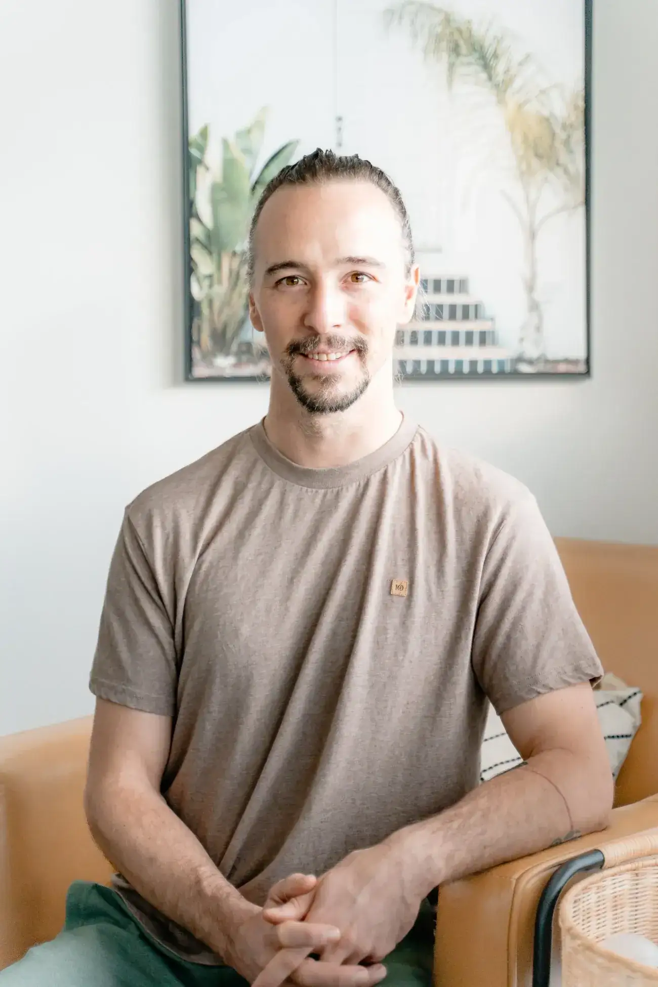 Dr. Will Tanner, acupuncturist and RMT, smiling in a tan leather armchair with his hands loosely clasped
